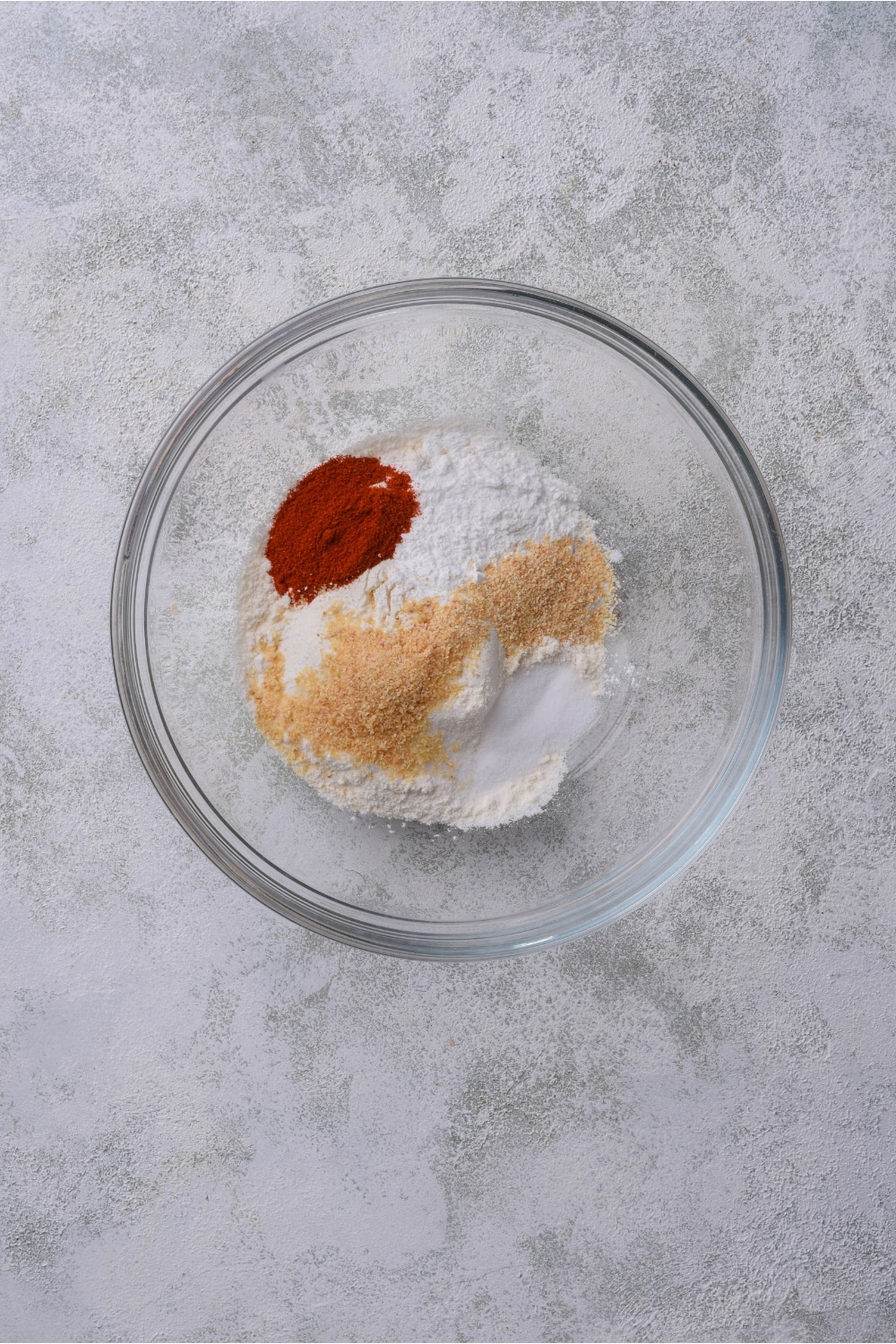 Paprika, flour, seasonings, and baking powder in a glass bowl on a counter.