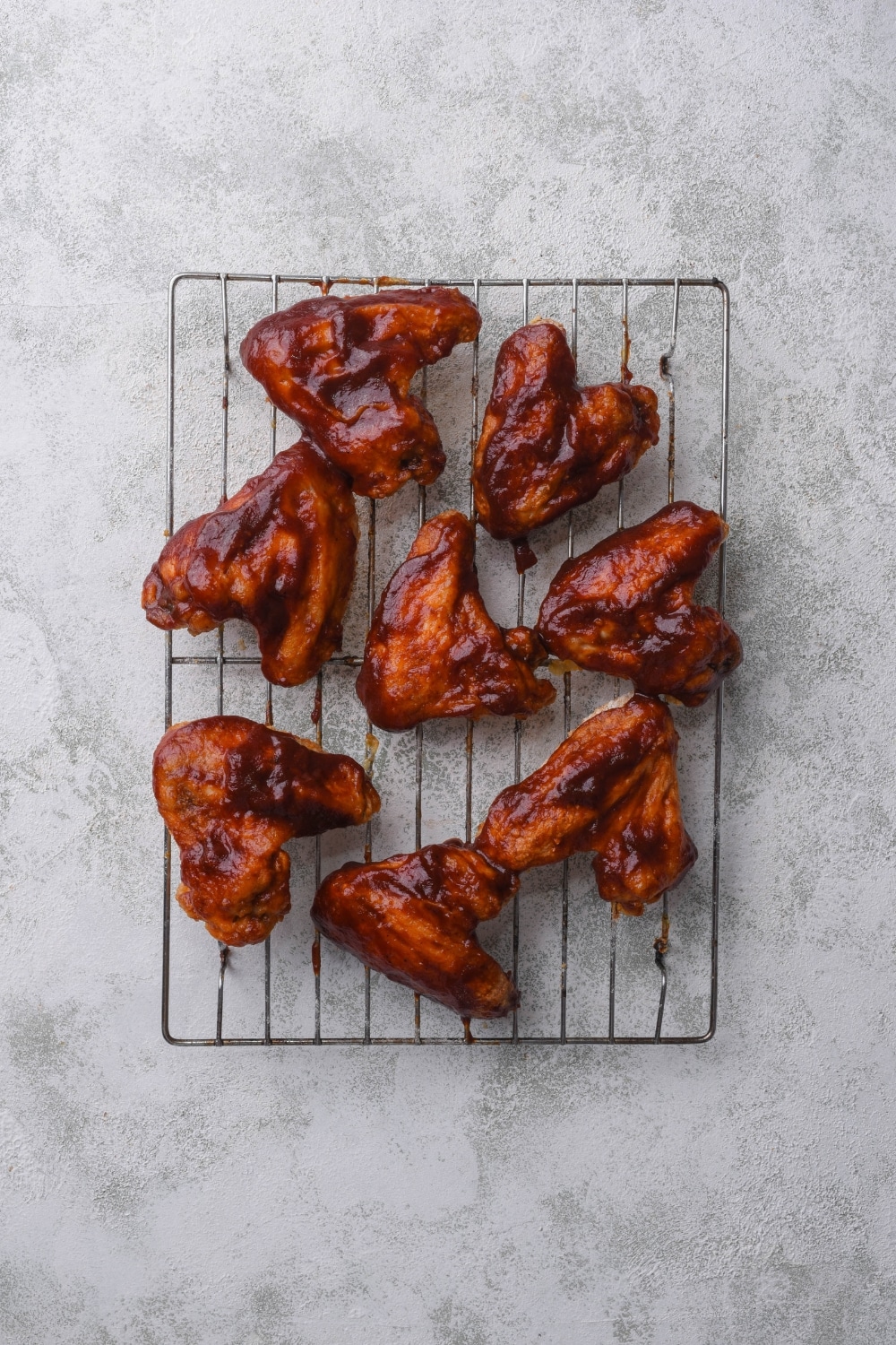 A bunch of bbq chicken wings on top of a wire rack on a grey counter.