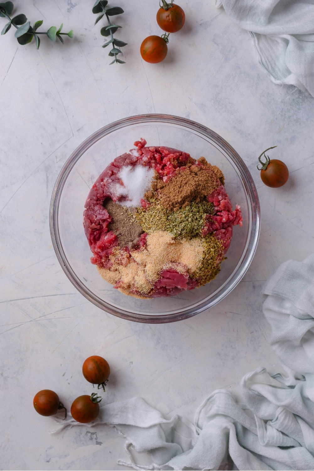 A bowl of raw ground beef with spices on top but not yet mixed together.