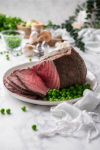 Sliced sirloin tip roast served with green peas on a plate.