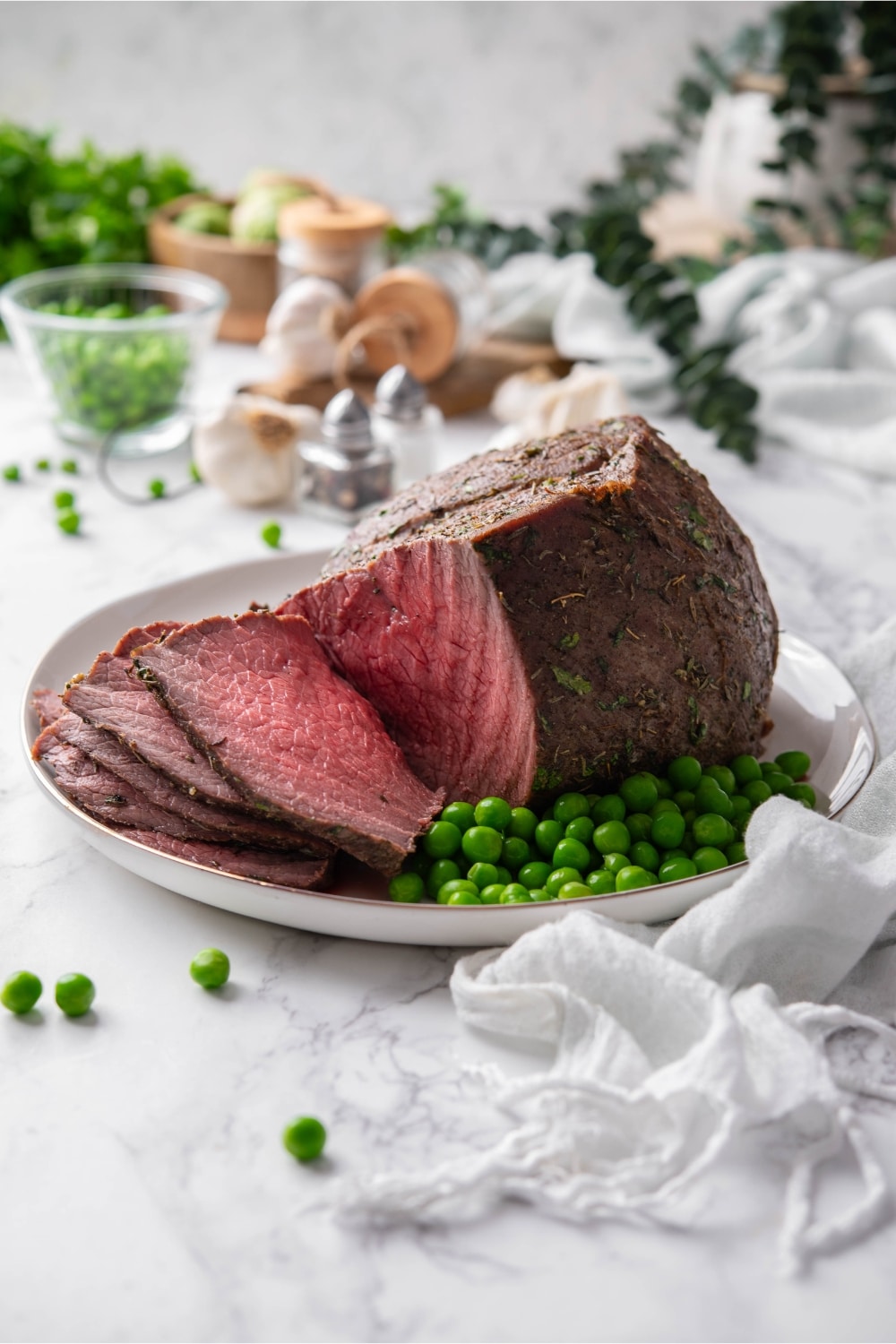 Sliced sirloin tip roast served with green peas on a plate.