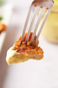 A fork holding a bite of breaded chicken coated in a yellow sauce.