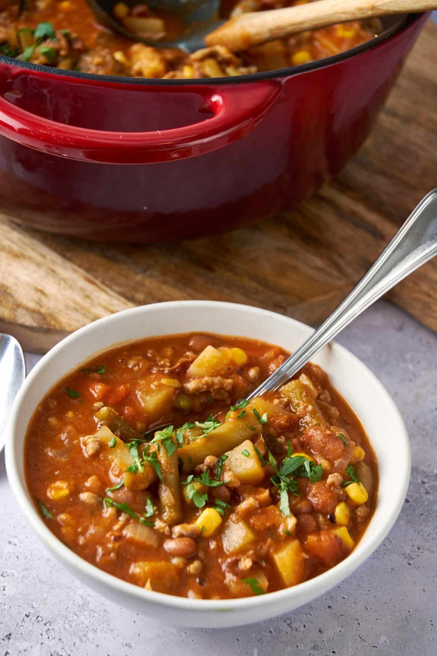 Cowboy soup in a bowl with a spoon. Part of a pot of cowboy soup is in the back.