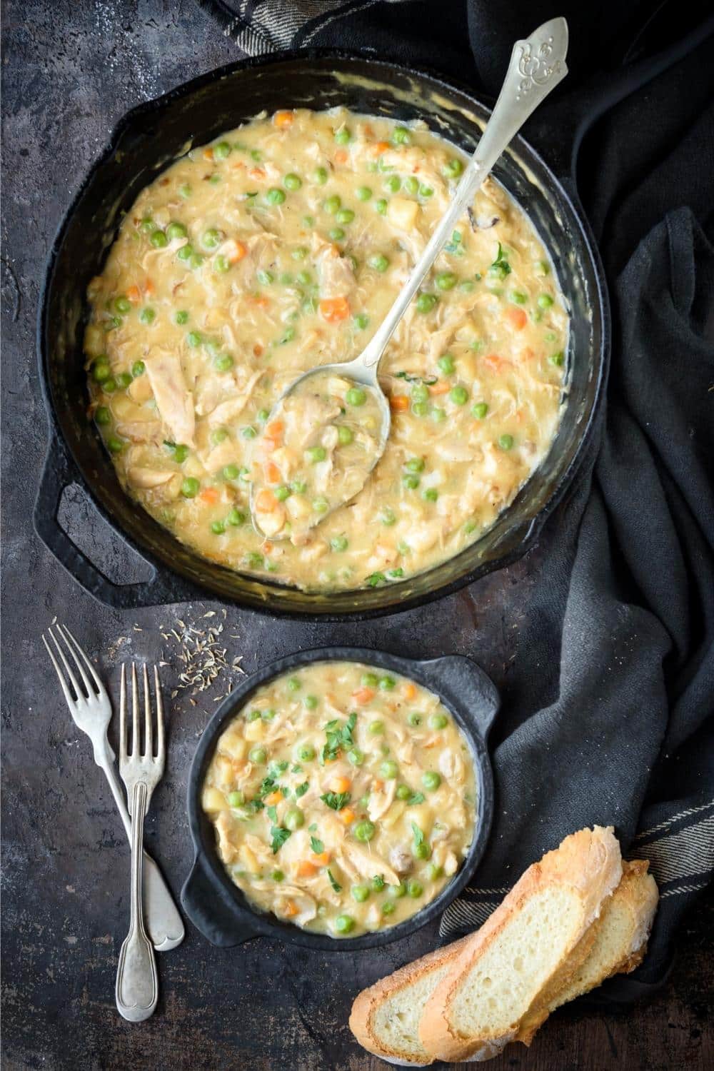 A large pot and smaller serving pot of crustless chicken pot pie, a serving spoon, forks, and sliced bread.