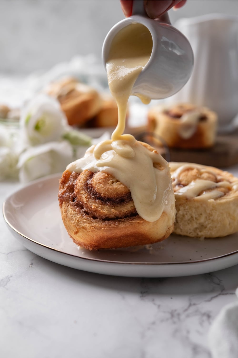 Pouring icing over protein cinnamon rolls on a plate.