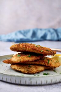 Four cooked turkey cutlets stacked together on a plate and garnished with fresh herbs.