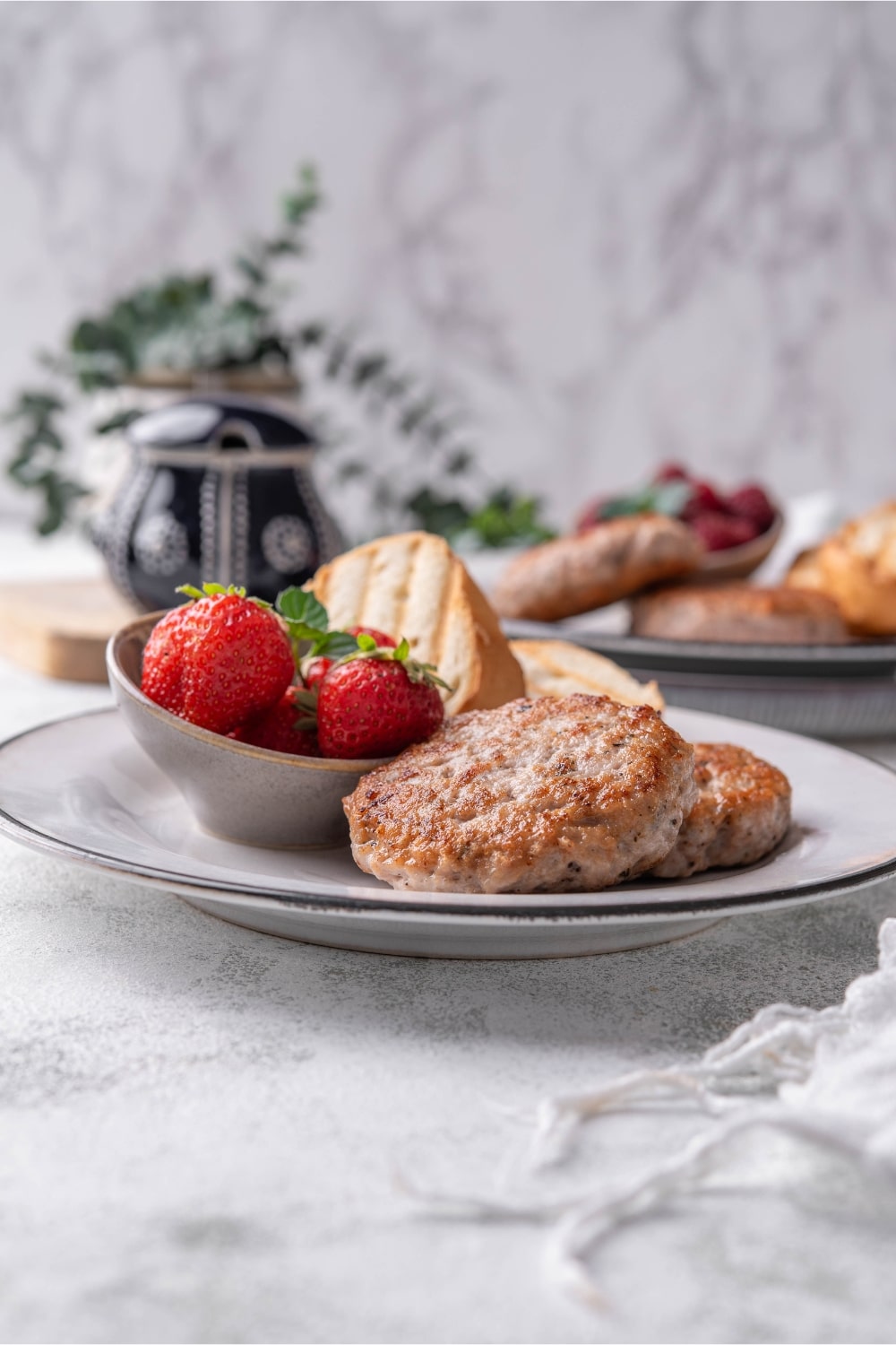 A turkey sausage breakfast plate with toasted baguette slices and a small bowl of strawberries.