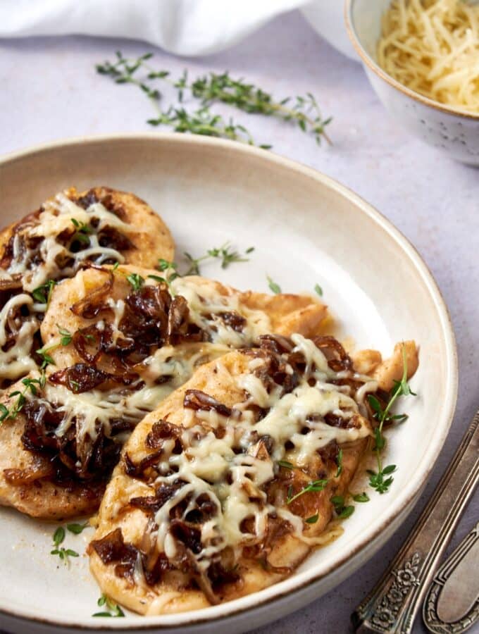 A plate of French onion chicken garnished with fresh thyme.