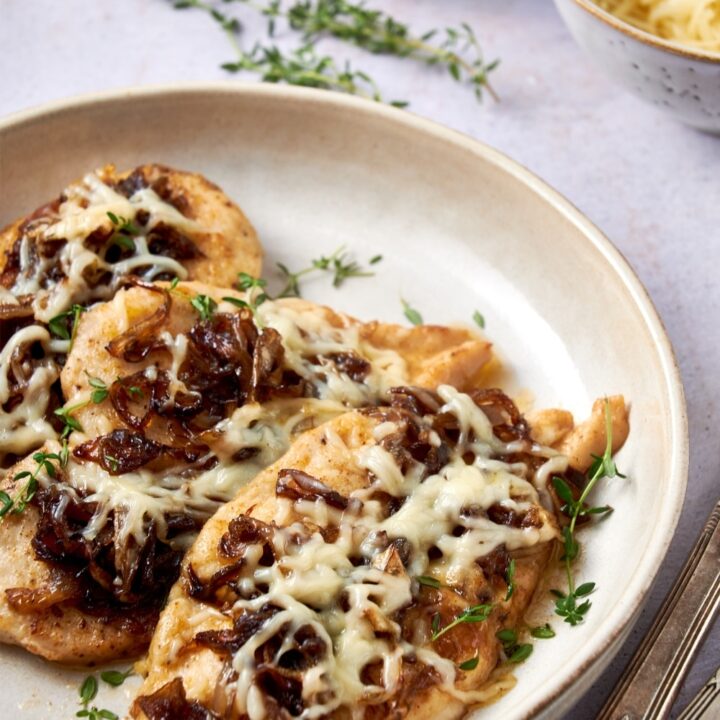 A plate of French onion chicken garnished with fresh thyme.