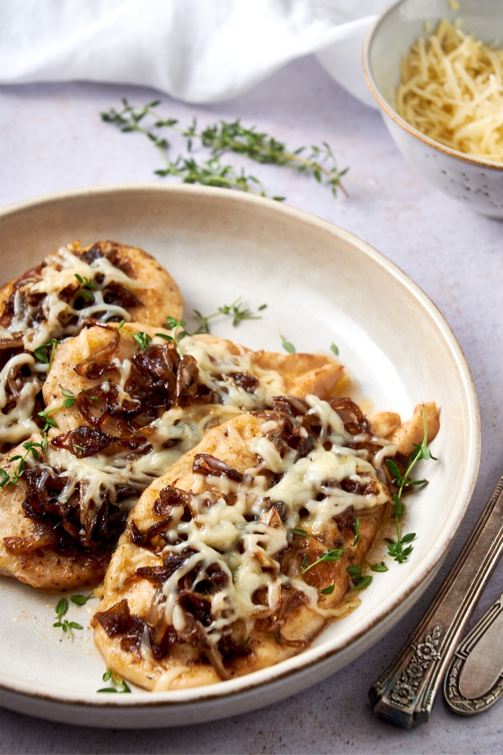 A plate of French onion chicken garnished with fresh thyme.