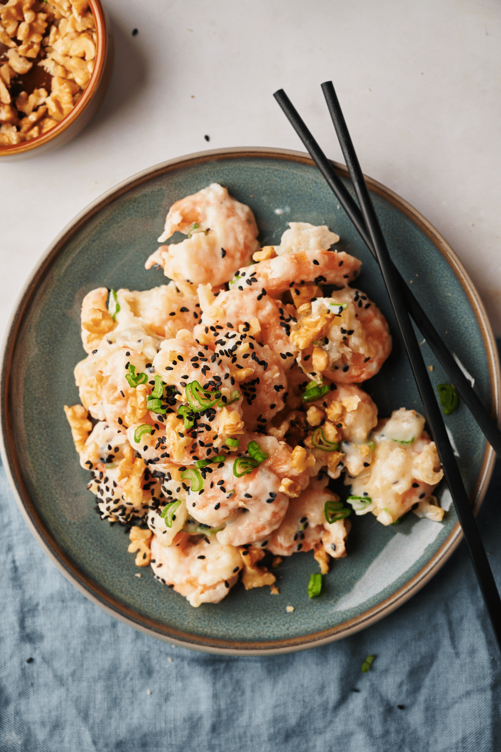 A plate of honey walnut shrimp garnished with sesame seeds, sliced green onions, and walnuts. A set of chopsticks is on the plate.