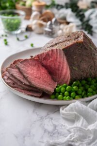 Sliced medium rare sirloin tip roast on a plate with green peas.