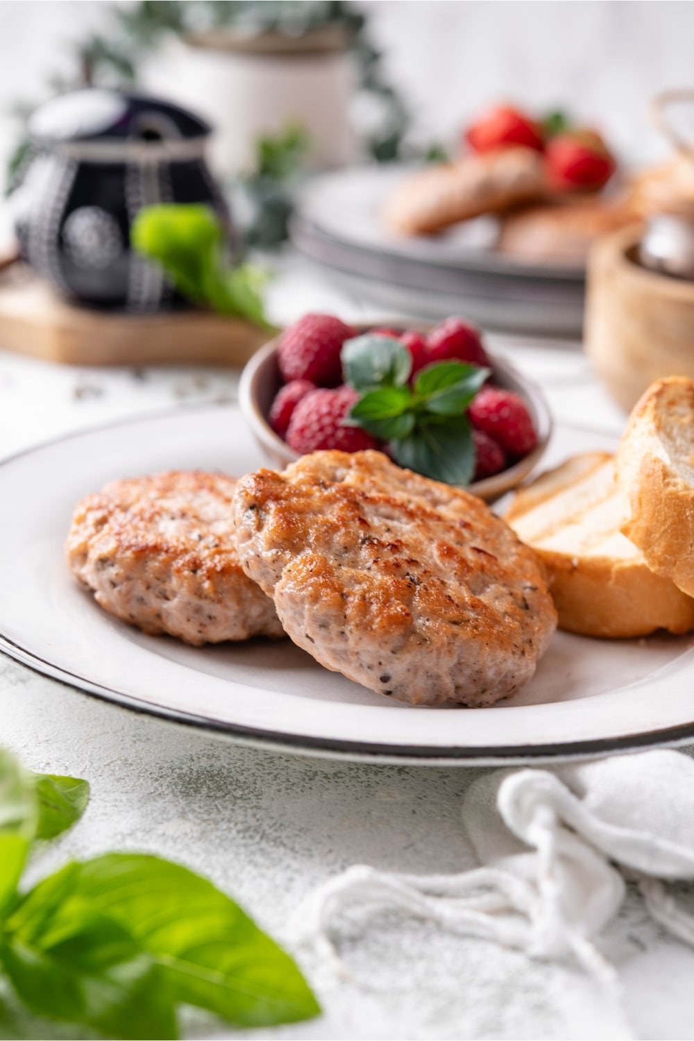 Two turkey sausage patties served with toasted baguette slices and raspberries.