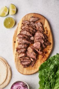 Sliced flank steak on a wooden cutting board on a grey counter.