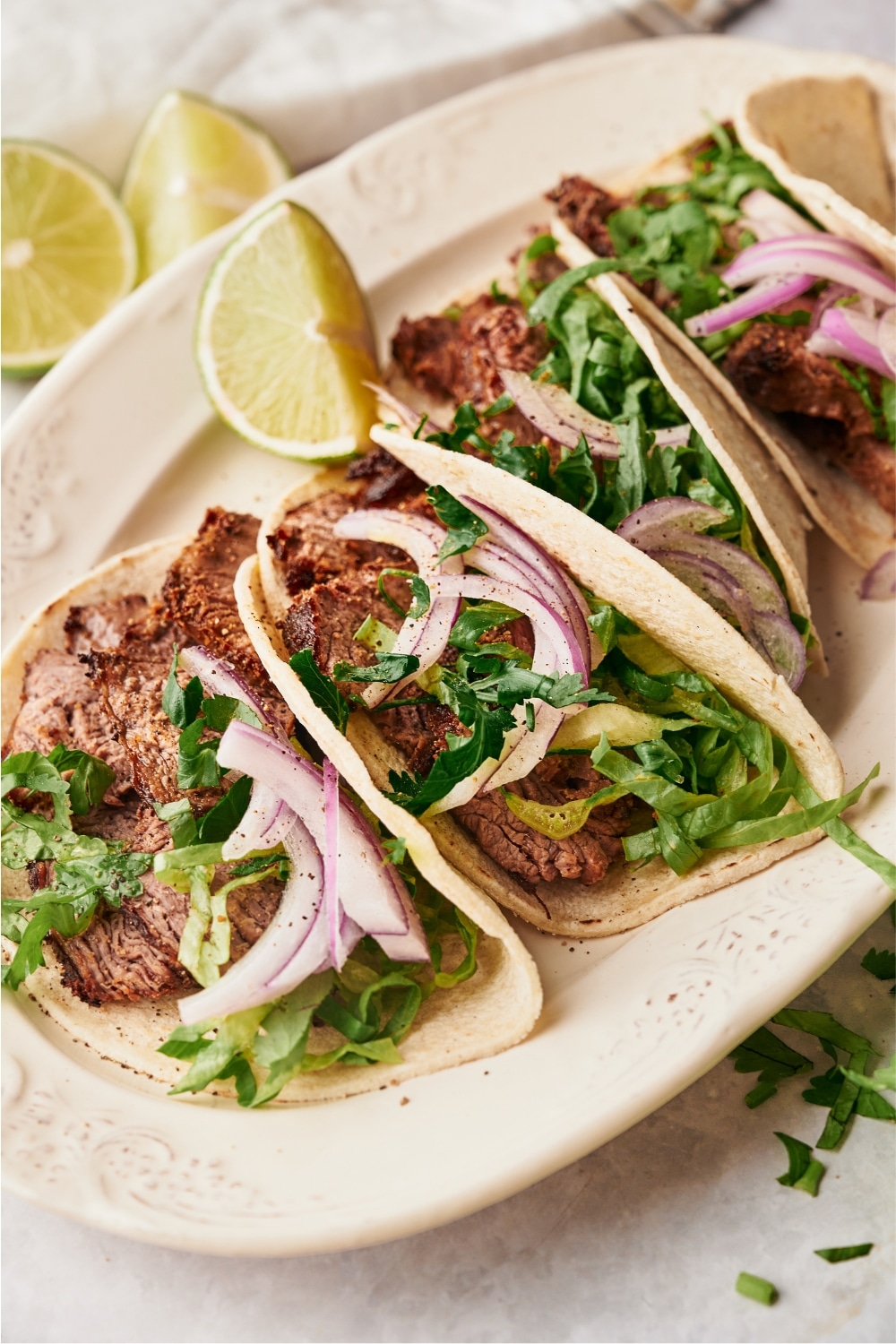 A couple of steak tacos with red onion and cilantro in the tortillas on a white plate.