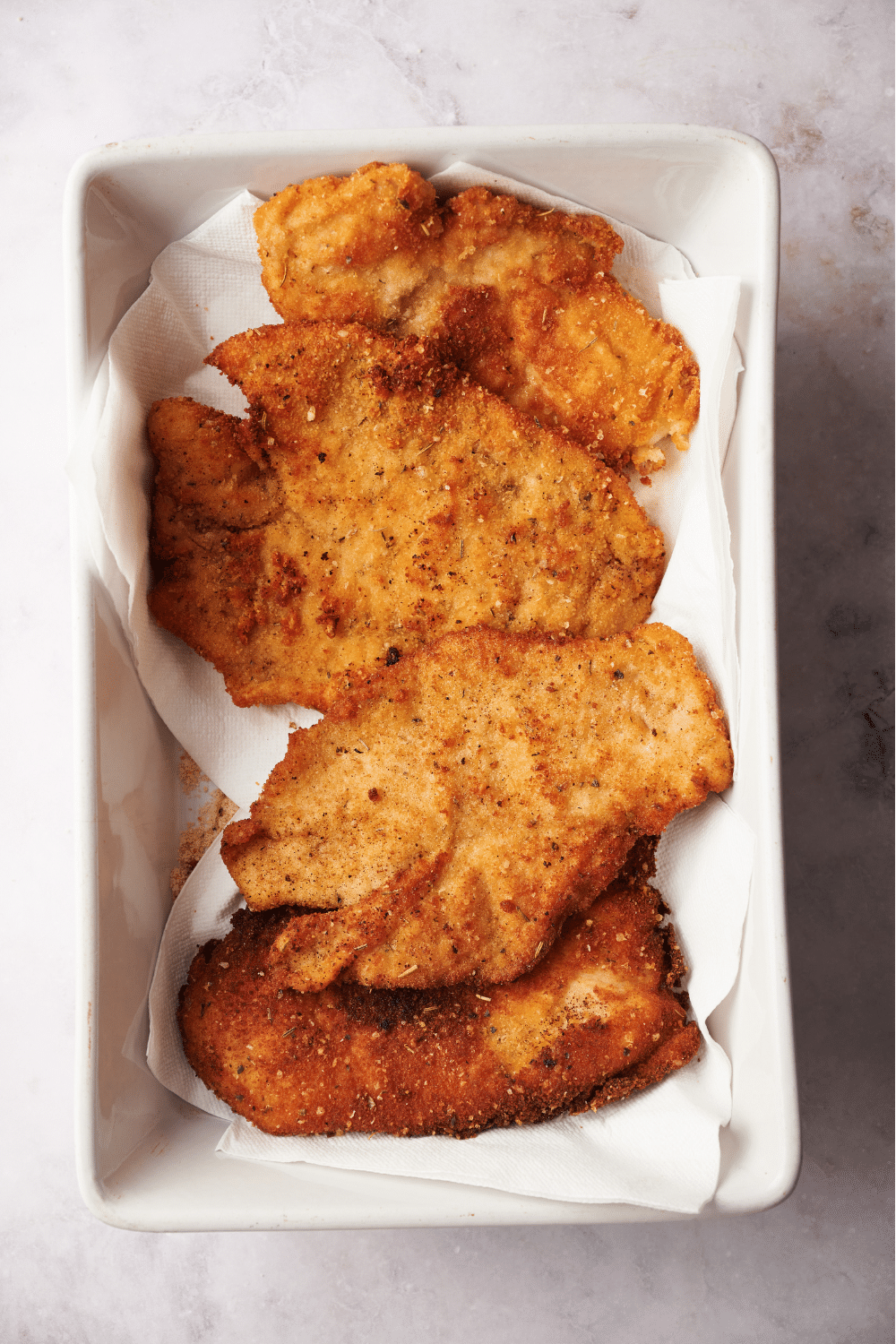 A serving dish lined with paper towels with four breaded chicken cutlets in it.