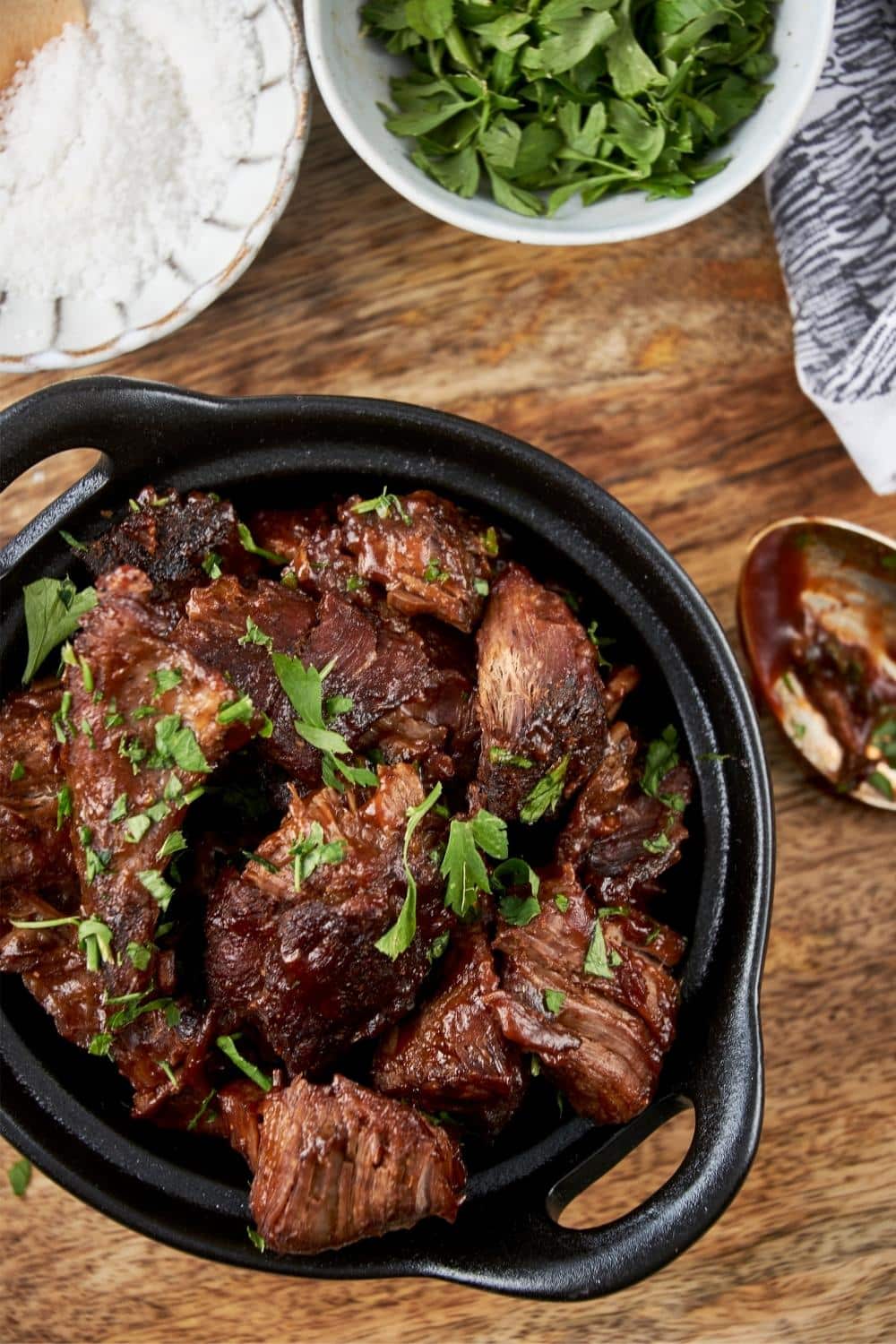 Overhead view of burnt ends in a small cast iron bowl garnished with fresh parsley.