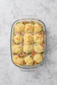 A glass casserole dish full of cooked chicken casserole. Twelve golden brown drop biscuits are on top.