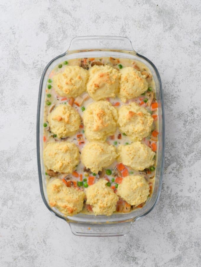 A glass casserole dish full of cooked chicken casserole. Twelve golden brown drop biscuits are on top.