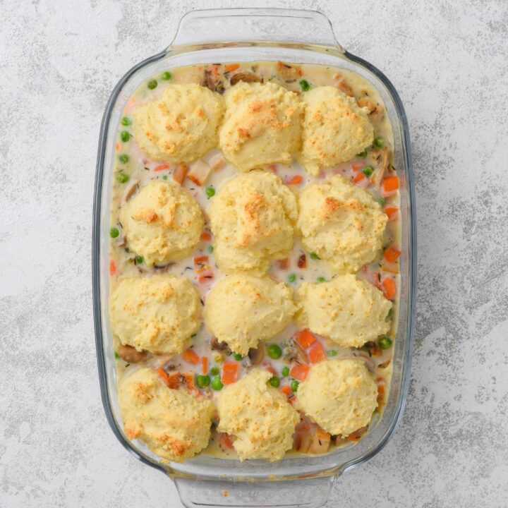 A glass casserole dish full of cooked chicken casserole. Twelve golden brown drop biscuits are on top.