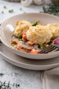 Part of a bowl with three biscuits on top of carrots, mushrooms, peas, and chicken in a creamy sauce.
