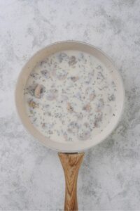 Mushrooms and seasonings simmering in a cream sauce in a white sauce pan.