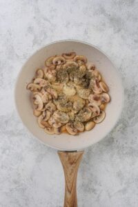 Cooked mushrooms coated in flour and seasonings in a white sauce pan.