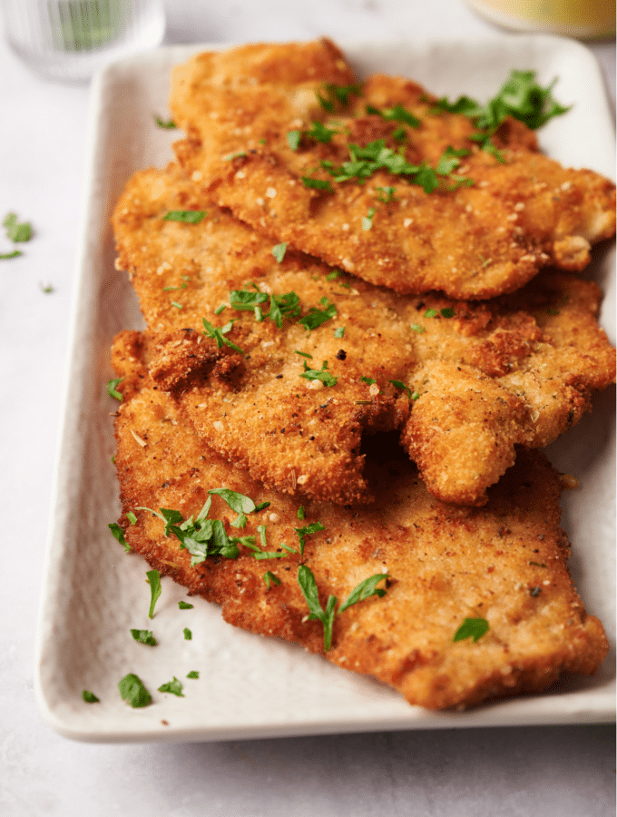 A serving dish lined with paper towels with three fried chicken cutlets in it, all garnished with fresh herbs.