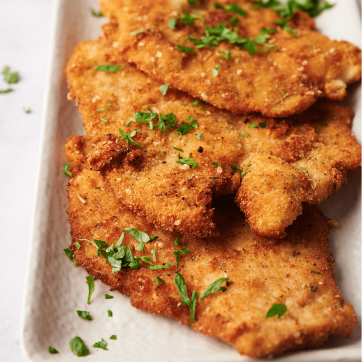 A serving dish lined with paper towels with three fried chicken cutlets in it, all garnished with fresh herbs.