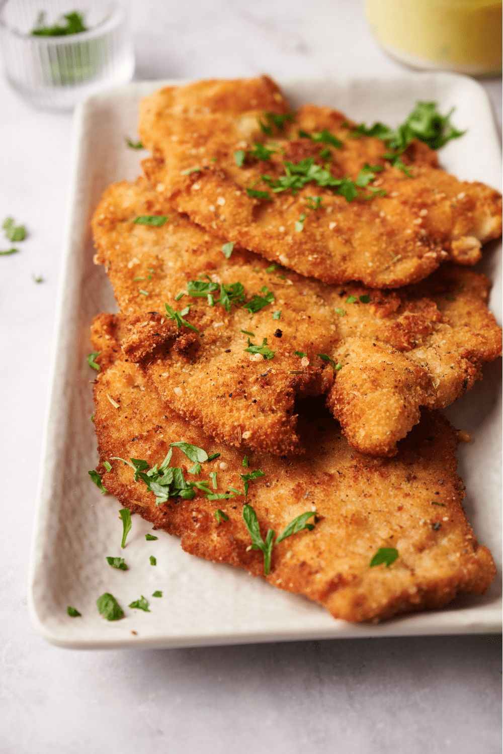 A serving dish lined with paper towels with three fried chicken cutlets in it, all garnished with fresh herbs.