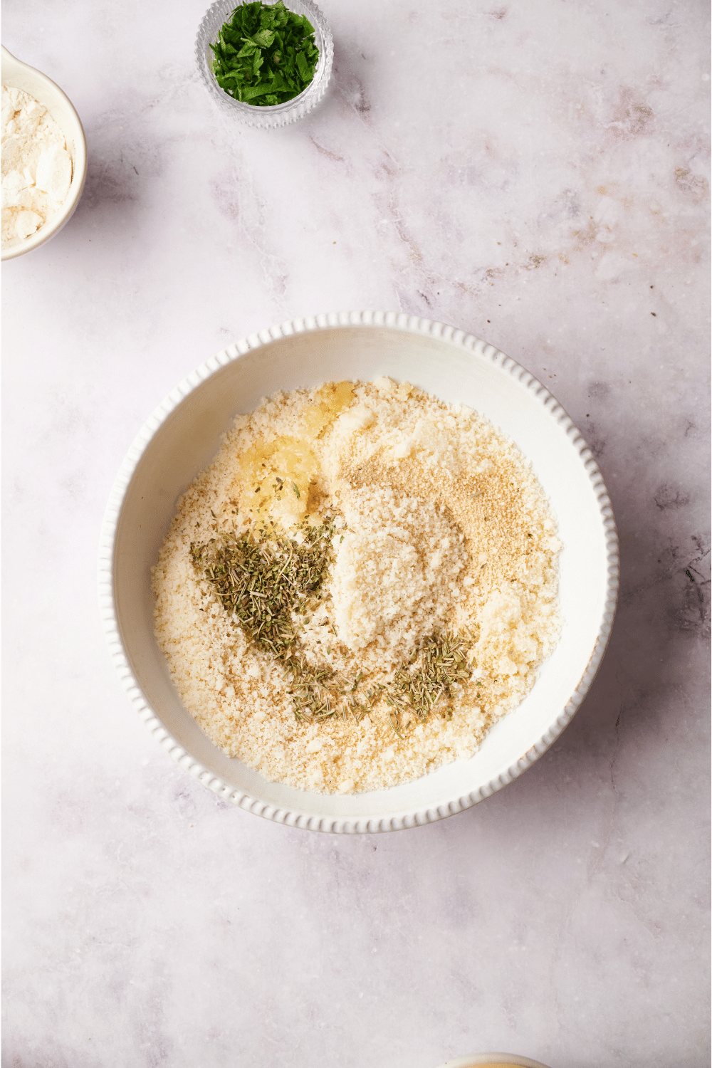 A bowl filled with grated parmesan cheese, herbs, and breadcrumbs.