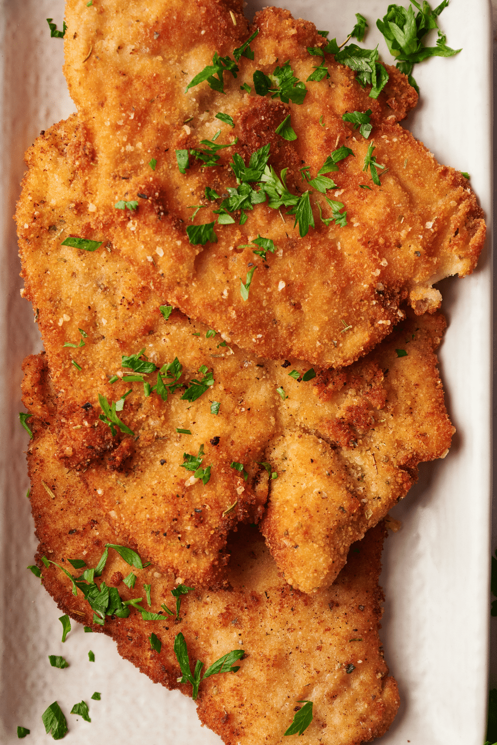 Three chicken cutlets overlapping one another on top of a baking dish.