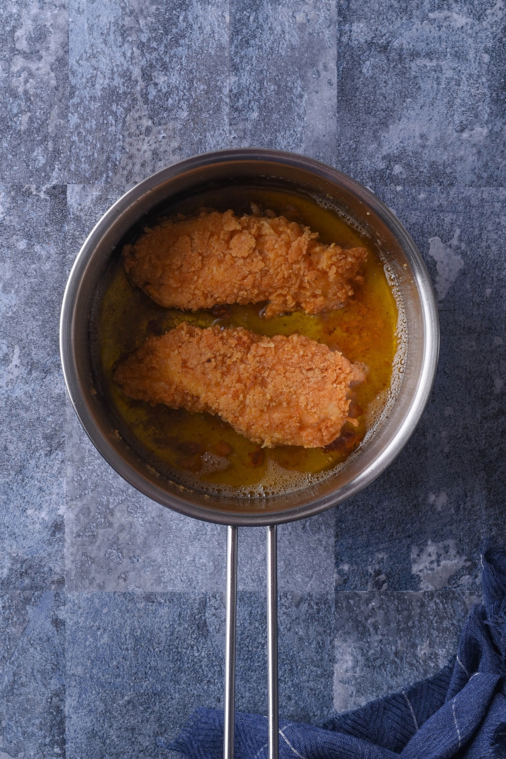 Two pieces of chicken frying in a pot of oil.