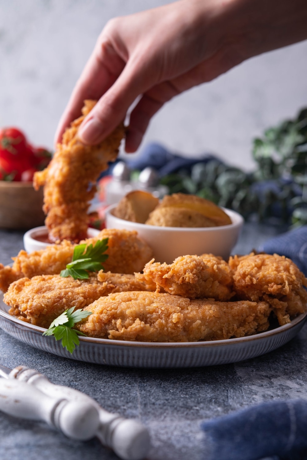 A hand dipping a chicken finger into ketchup. In front of that are four chicken fingers on a grey plate.