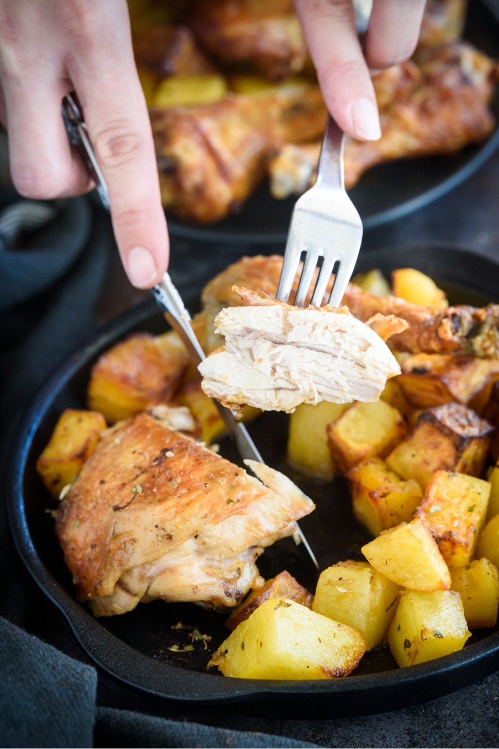 A piece of chicken on a fork over a plate with chicken and potatoes.