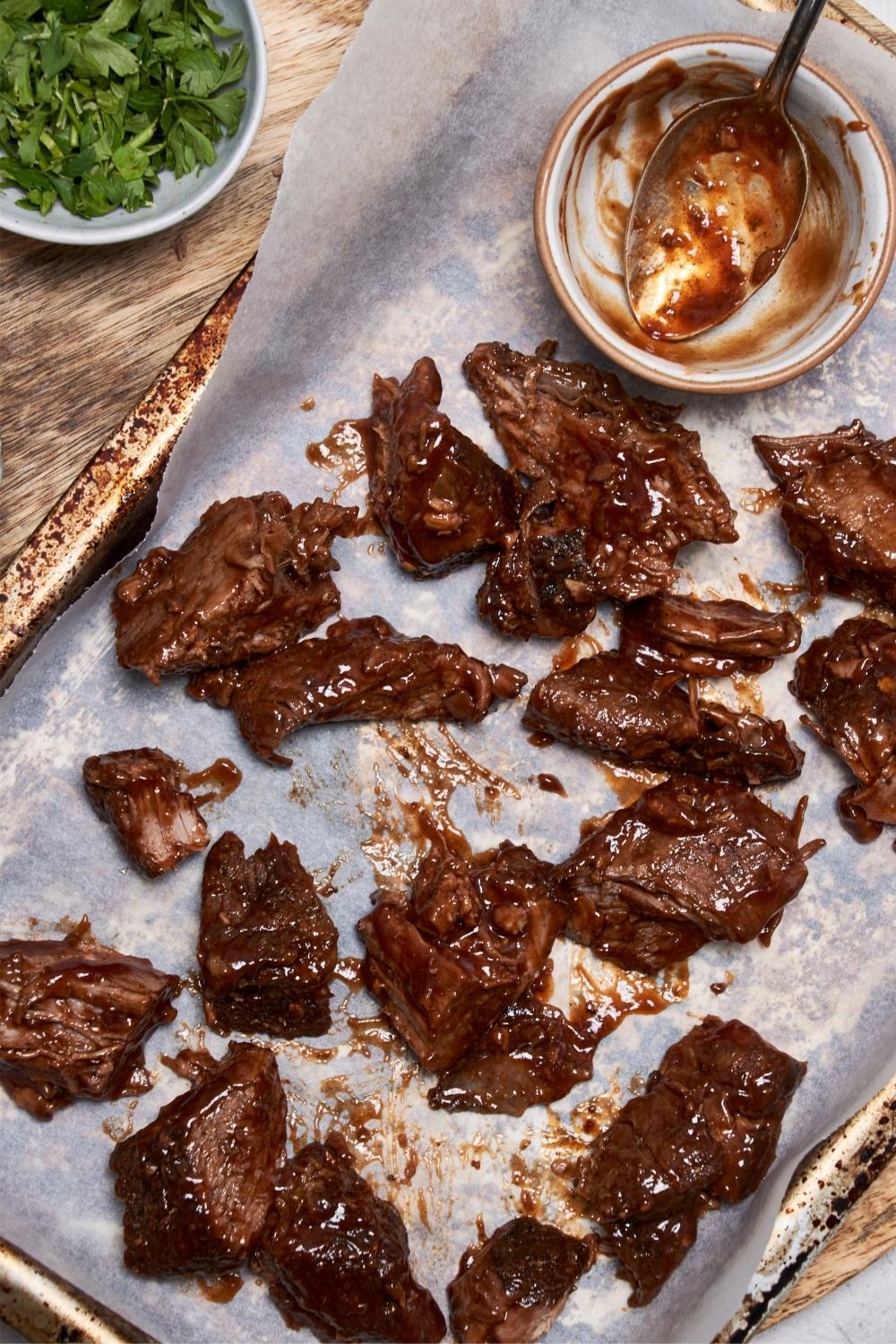 Burnt ends covered with bbq sauce on a baking sheet, next to an emptied bowl of sauce with a spoon.