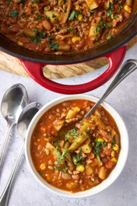 A bowl of cowboy soup with a spoon next to a large pot of cowboy soup.