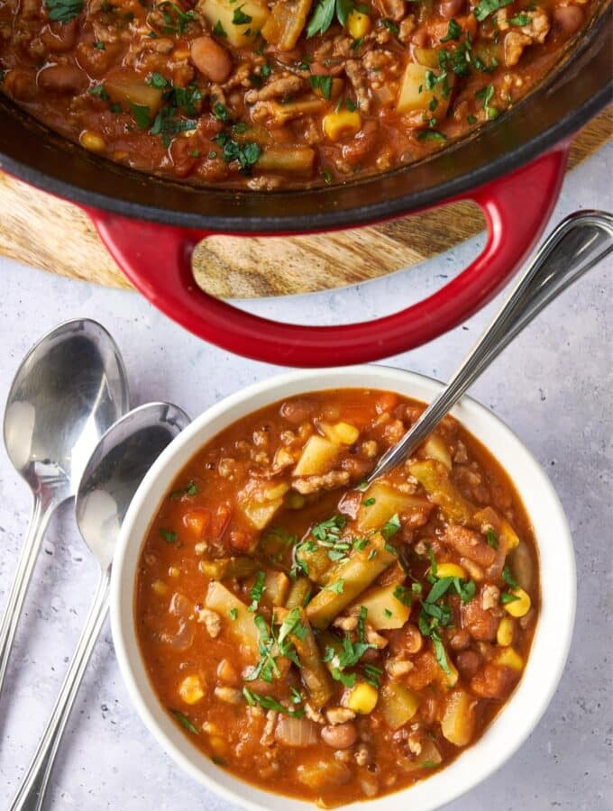 A bowl of cowboy soup with a spoon next to a large pot of cowboy soup.