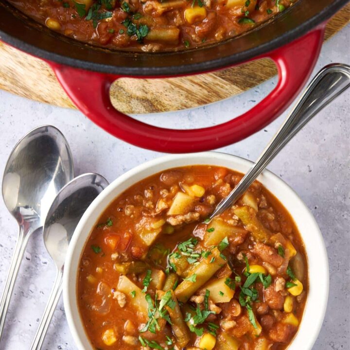 A bowl of cowboy soup with a spoon next to a large pot of cowboy soup.