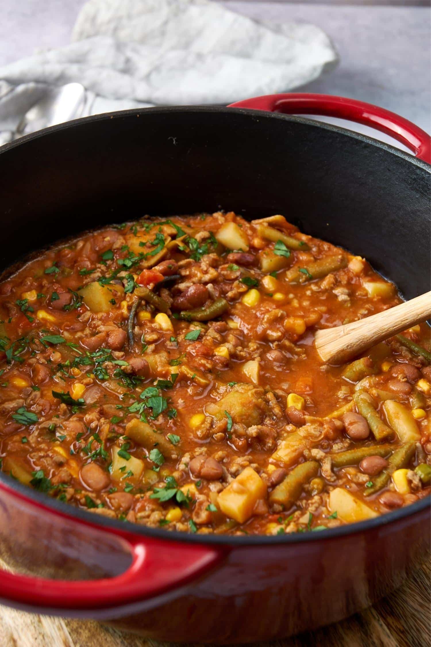 A closer look at a large red pot of cowboy soup with a wooden spoon.