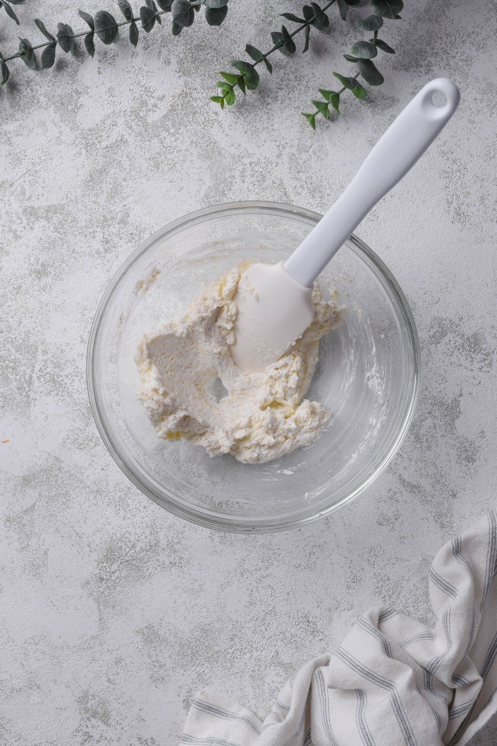 A rubber spatula in a glass bowl that has a cream cheese mixture in it.