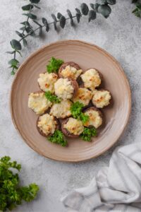 A bunch of cream cheese stuffed mushrooms on top of a plate on a grey counter.