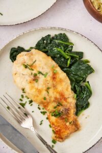 A piece of mushroom baked chicken on top of collard greens on a plate.