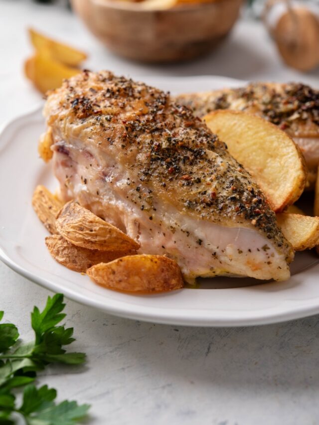 Two seasoned chicken breasts on a plate with potato wedges.