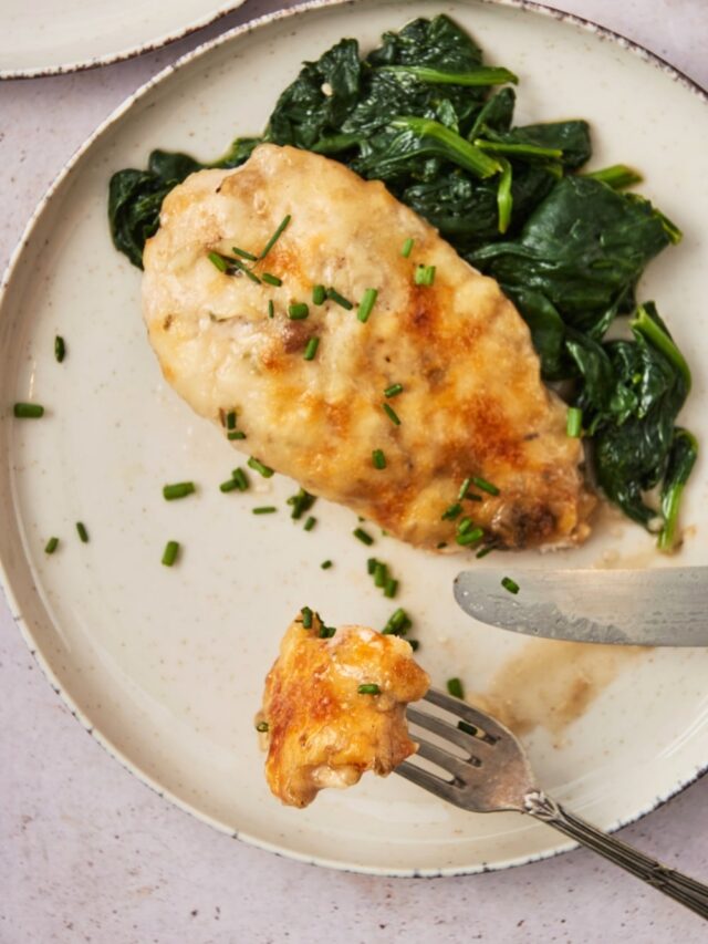 A fork with a piece of chicken on it on a plate with the rest of the chicken breast on the plate.