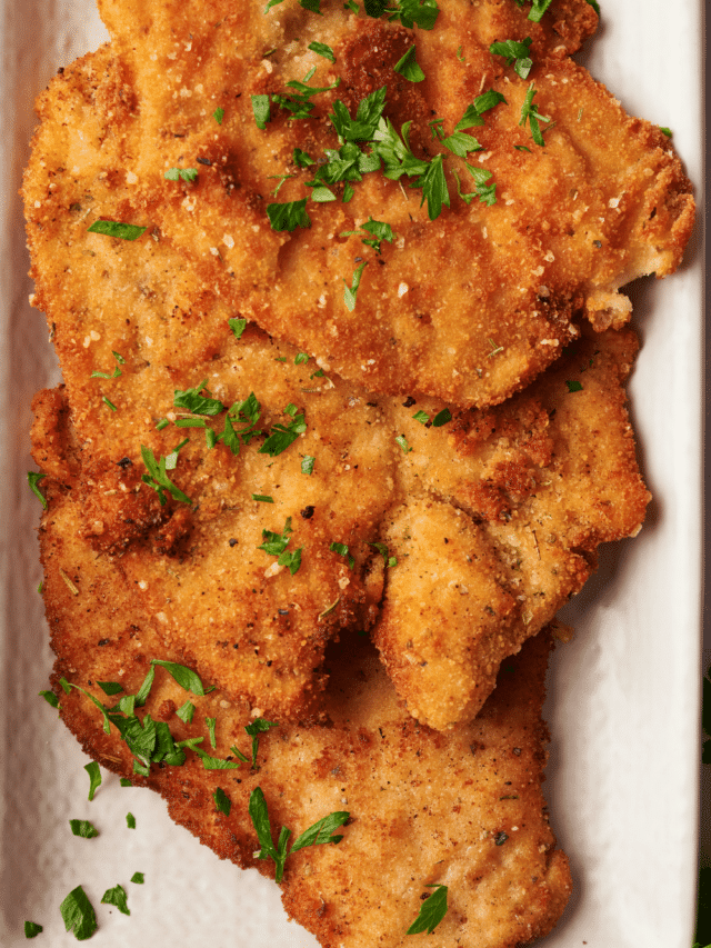 Three chicken cutlets overlapping one another on top of a baking dish.