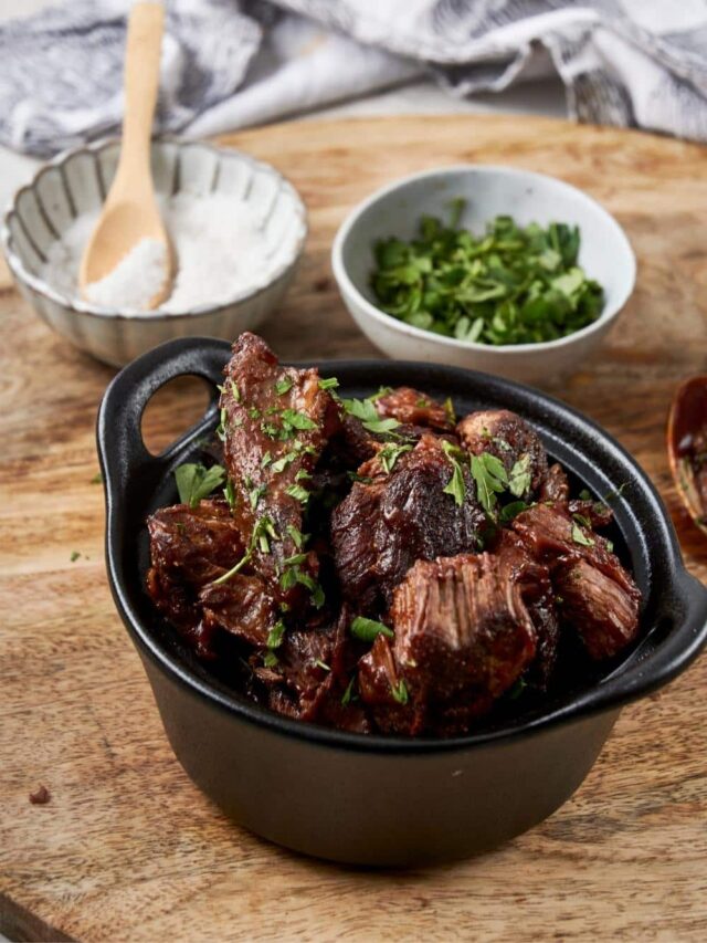 Burnt ends topped with fresh parsley in a small cast iron bowl, next to bowls of salt and parsley.