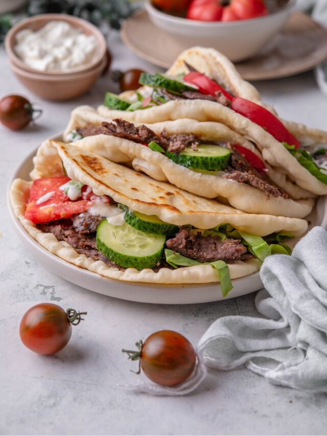 A gyro with tomato, cucumber, and sliced beef with two gyros behind them.