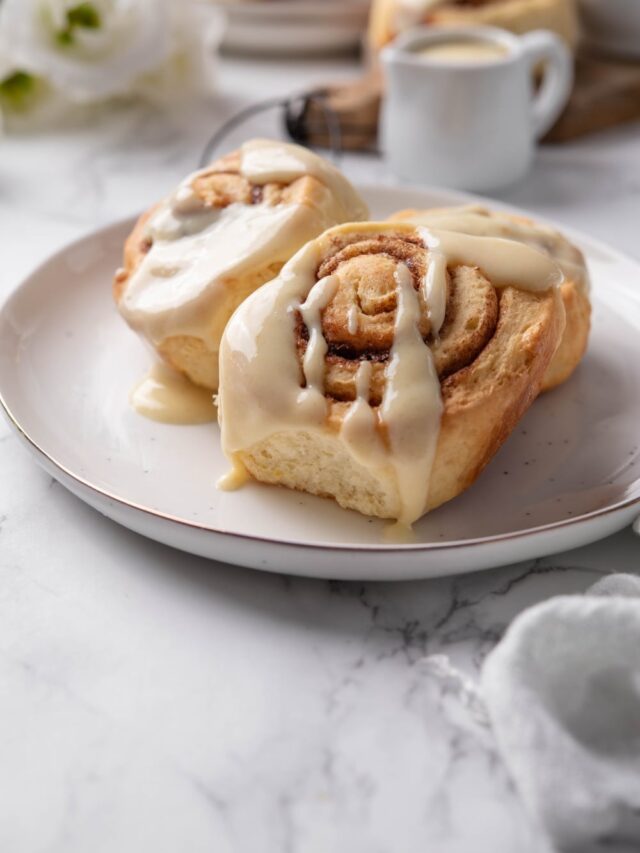 Three protein cinnamon rolls drizzled with icing on a plate.