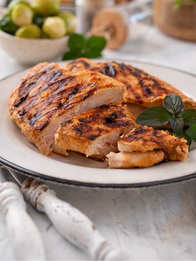 Sliced grilled chicken breasts garnished with fresh herbs on a white plate.